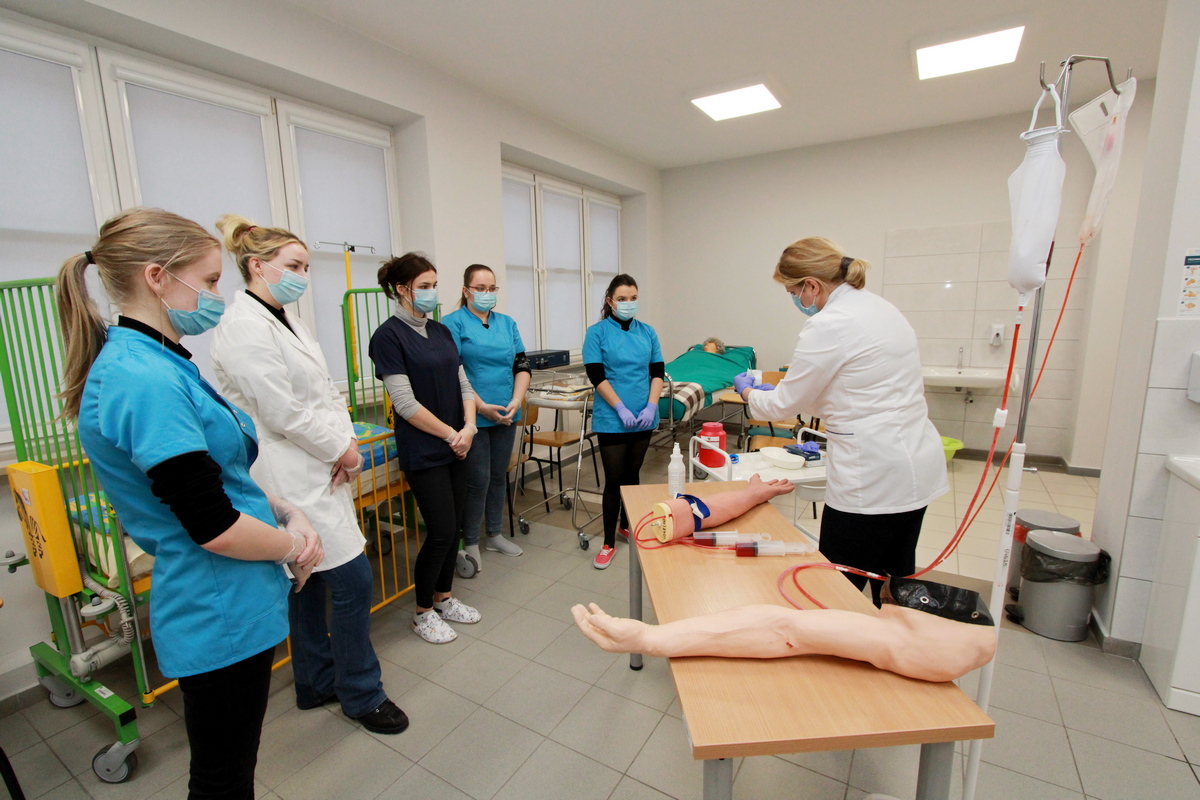 Na zdjęciu prowadzący zajęcia objaśnia studentom zasady postępowania przy wykonywaniu czynności pielęgniarskich